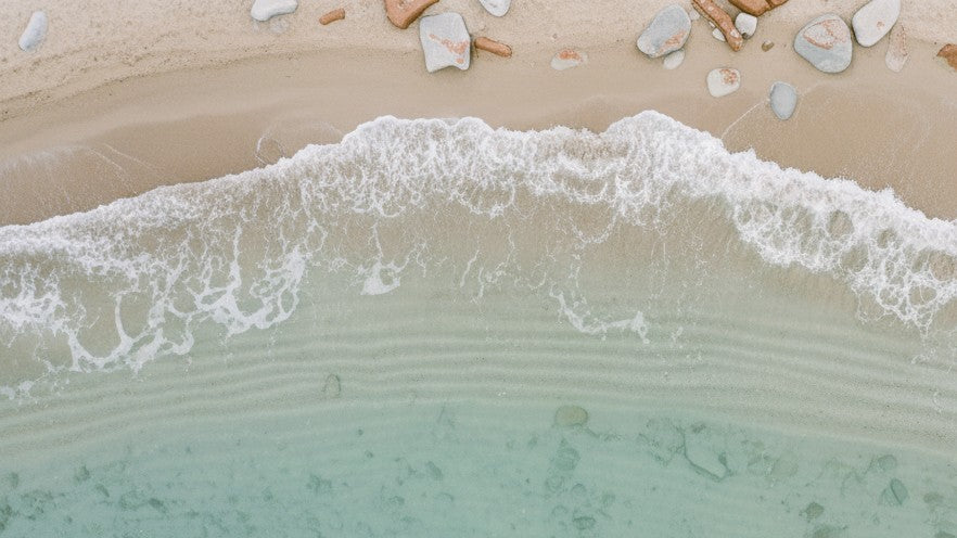 Top-down view of waves crashing onto a sandy beach with pebbles.
