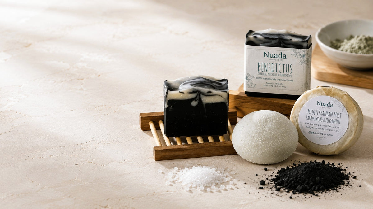 Nuada Benedictus soap bar and Mediterranean Mist Sea Salt Soap set displayed on a light beige surface with sea salts, powder, and a wooden soap dish.