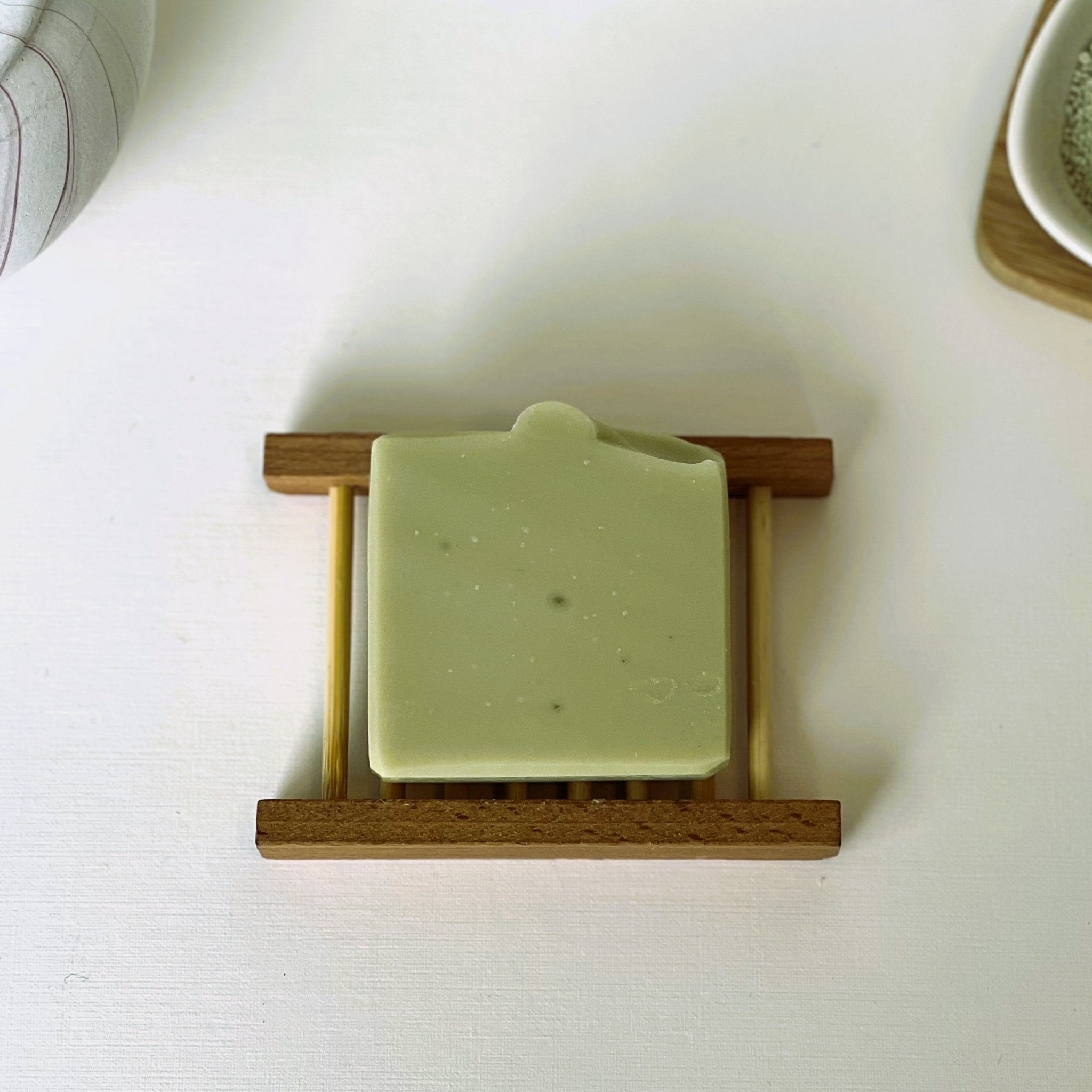Top-down view of Nuada Naturals Deep Forest green soap bar on wooden dish