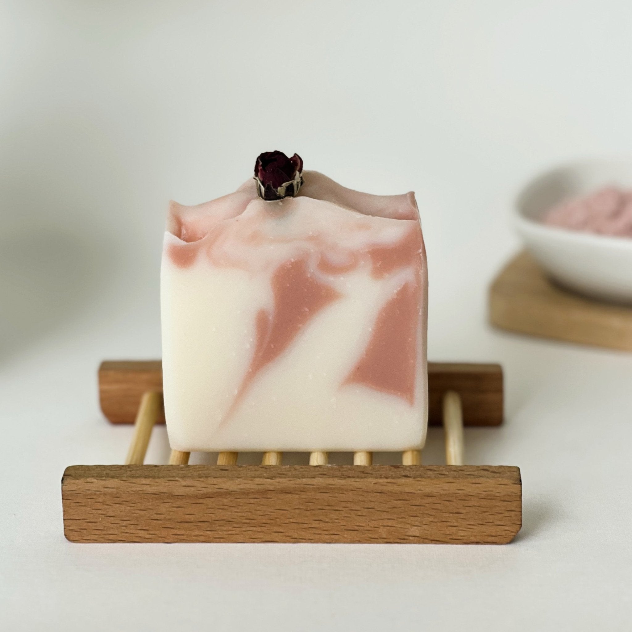 Nuada Naturals Rita's Petals pink swirl soap bar topped with dried rosebud on wooden dish